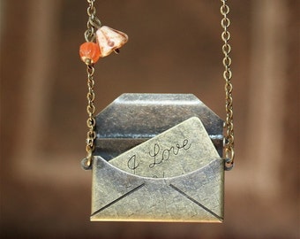 May include: A gold chain necklace with a small envelope charm. The envelope is open and has a handwritten note inside that says "I Love You". The necklace also has two small orange and white beads.
