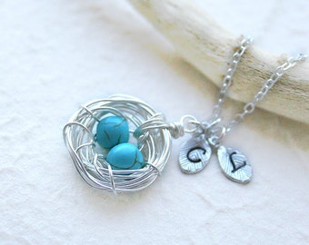 May include: Silver necklace with a wire bird's nest charm containing two turquoise blue stones. The necklace has two silver charms with the letters 'C' and 'V' on them.