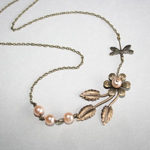 May include: A delicate gold necklace with a floral pendant featuring a pearl center and three leaves. The necklace also includes a dragonfly charm and three small pearls.