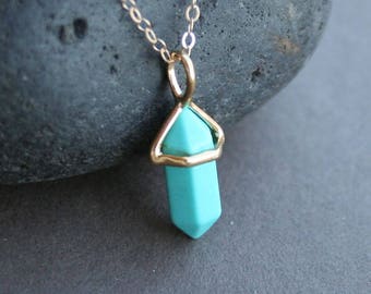 May include: A gold chain necklace with a turquoise crystal pendant in the shape of a point. The crystal is set in a gold frame.