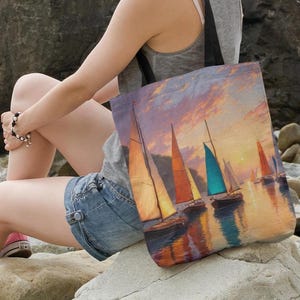 May include: A tote bag featuring a painting of sailboats on the water at sunset. The sailboats have orange, teal, and white sails. The sky is a mix of orange, pink, and purple hues. The bag has black straps.