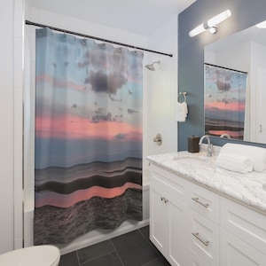 May include: A shower curtain featuring a sunset scene with pink, blue, and gray hues. The design depicts a wavy horizon line and cloudy sky, creating a serene and artistic bathroom accessory.