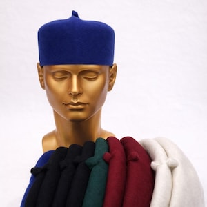Pu&ograve; includere: Esposizione di cappelli fez colorati, tra cui blu, nero, verde, bordeaux e bianco. I cappelli sono esposti su una testa di manichino dorata. Il testo "Elitebystyle" &egrave; nell'angolo in alto a sinistra.