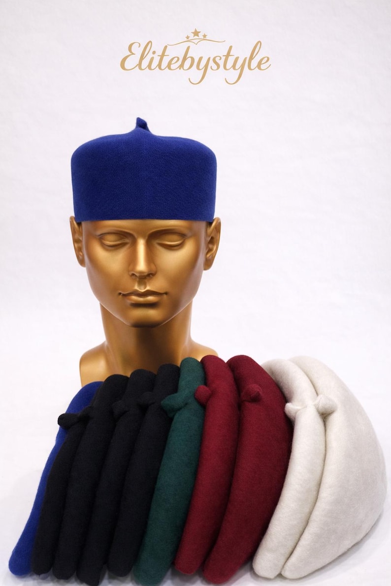 Pu&ograve; includere: Esposizione di cappelli fez colorati, tra cui blu, nero, verde, bordeaux e bianco. I cappelli sono esposti su una testa di manichino dorata. Il testo "Elitebystyle" &egrave; nell'angolo in alto a sinistra.