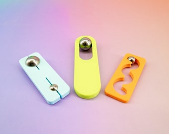 May include: Three colorful wooden toys with metal balls. One is light blue with a slit, another is yellow with a hole, and the third is orange with a wavy cutout. The background has a gradient of colors.