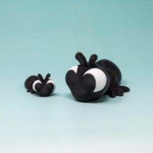 Puede incluir: Dos hormigas de juguete de plástico negro con grandes ojos blancos. La hormiga más grande está mirando a la más pequeña.