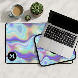 May include: A laptop rests on a matching iridescent mousepad and laptop sleeve. The mousepad features a black border and a large black circle with the letter "M". A cup of coffee and potted succulents are also visible.