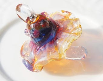 May include: A colorful glass sculpture of a small animal, possibly a bear or a rabbit, with a rounded body and a small, clear ear. The sculpture features a mix of colors, including red, blue, yellow, and orange.