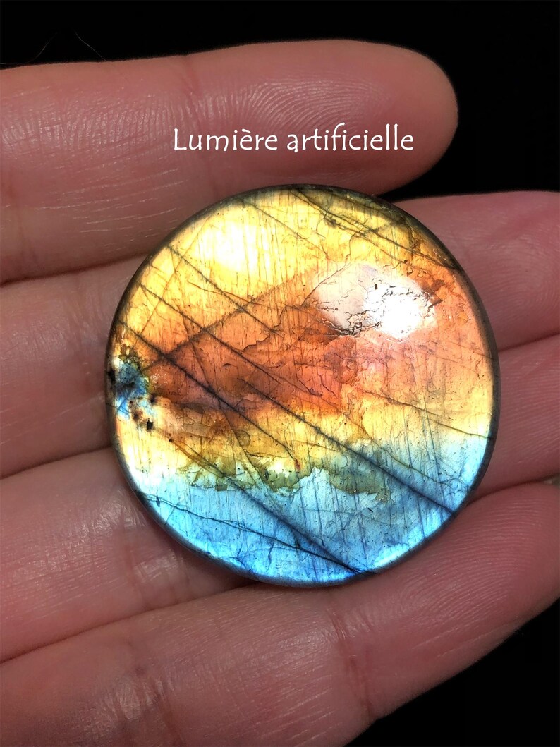 May include: A round, polished gemstone with a vibrant color gradient. The stone transitions from blue at the bottom to orange and yellow in the center, with dark lines across the surface. The text "Lumi&egrave;re artificielle" is visible.