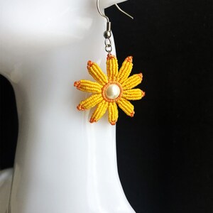 May include: Yellow and orange flower-shaped earrings with a pearl center. The earrings are made of string and have a silver hook.