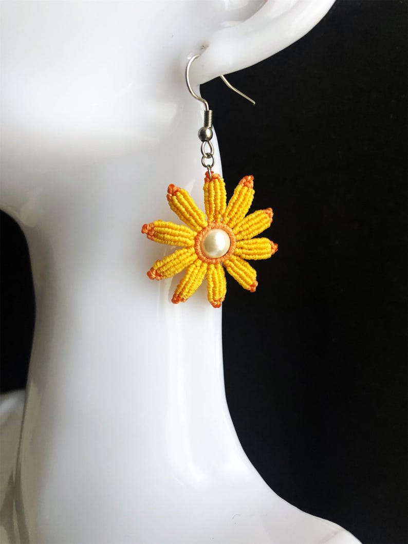 May include: Yellow and orange flower-shaped earrings with a pearl center. The earrings are made of string and have a silver hook.