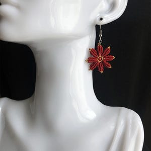 May include: Red flower-shaped earrings with a gold center. The earrings are hanging from a silver hook.