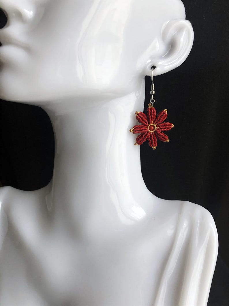 May include: Red flower-shaped earrings with a gold center. The earrings are hanging from a silver hook.