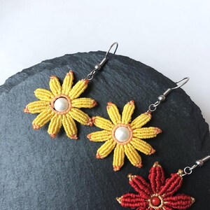 May include: Three pairs of flower-shaped earrings. Two pairs are yellow with a white pearl center and one pair is red with a gold center.