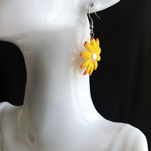 May include: Yellow and orange beaded flower dangle earrings with a pearl center. The earrings are on a white mannequin head.
