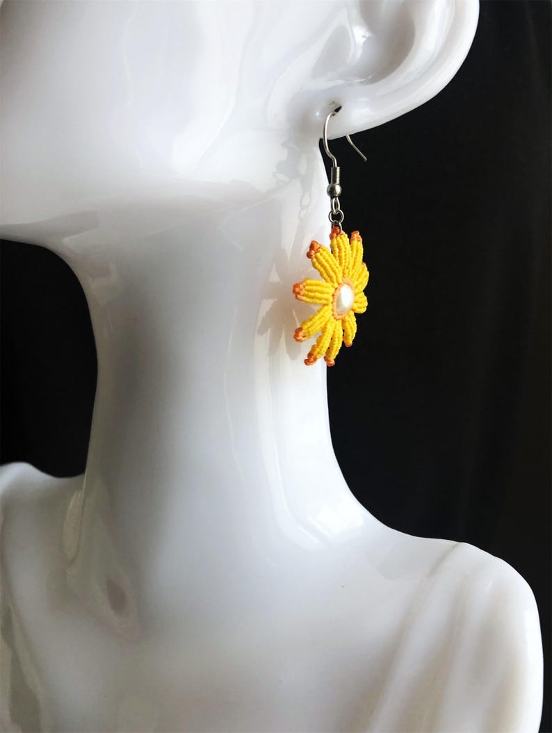 May include: Yellow and orange beaded flower dangle earrings with a pearl center. The earrings are on a white mannequin head.