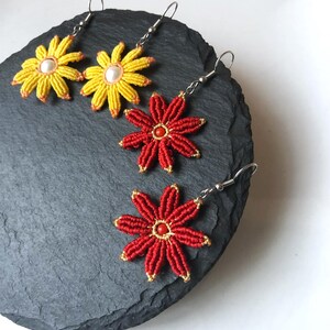 May include: Three pairs of flower-shaped earrings with silver hooks. Two pairs are yellow with white centers and one pair is red with a red center.