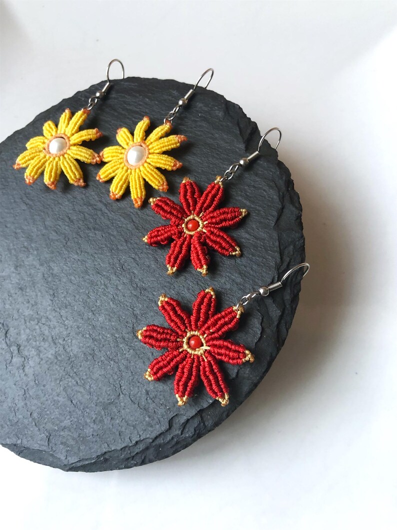 May include: Three pairs of flower-shaped earrings with silver hooks. Two pairs are yellow with white centers and one pair is red with a red center.