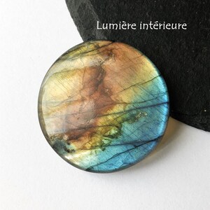 May include: A round, polished gemstone with a mix of colors including blue, brown, and yellow. The stone has a smooth surface and a natural, organic appearance. The text "Lumi&egrave;re int&eacute;rieure" is visible in white.