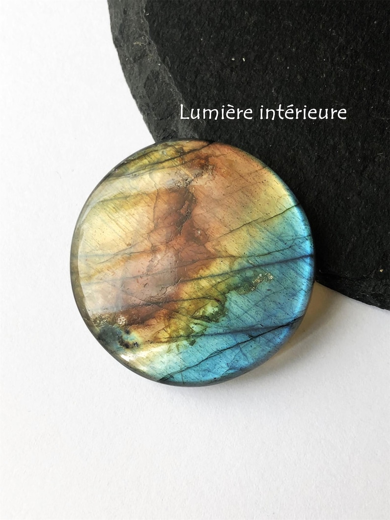 May include: A round, polished gemstone with a mix of colors including blue, brown, and yellow. The stone has a smooth surface and a natural, organic appearance. The text "Lumi&egrave;re int&eacute;rieure" is visible in white.