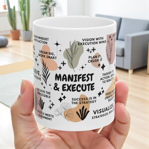 Könnte beinhalten: Weißer Keramikbecher mit dem Schriftzug "Manifest & Execute" in Schwarz, umgeben von inspirierenden Sätzen und Grafiken in Schwarz, Pfirsich und Grün. Der Becher wird von einer Hand gehalten.
