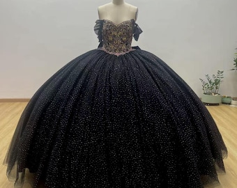 May include: A formal black ball gown with a sweetheart neckline and a full skirt. The bodice is embellished with gold and pink embroidery. The skirt is made of a black fabric with small, sparkling accents.