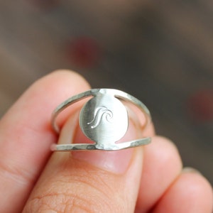 May include: A silver ring featuring a wave design on the front. The ring is open on the sides and has a hammered texture.