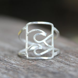 Peut inclure: Une bague en argent avec un motif géométrique composé de deux lignes courbes à l'intérieur d'un cadre rectangulaire.