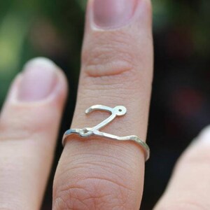 Op de afbeelding: Een zilveren ring met een zwierig letter 'Z' ontwerp. De ring wordt aan een vinger gedragen.