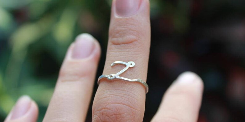 Op de afbeelding: Een zilveren ring met een zwierig letter 'Z' ontwerp. De ring wordt aan een vinger gedragen.