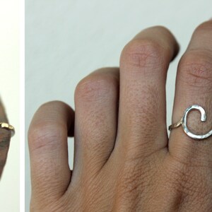 Op de afbeelding: Een zilveren ring met een gehamerde afwerking, in de vorm van een golf. De ring wordt aan een vinger gedragen.