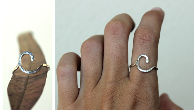 Op de afbeelding: Een zilveren ring met een gehamerde afwerking, in de vorm van een golf. De ring wordt aan een vinger gedragen.