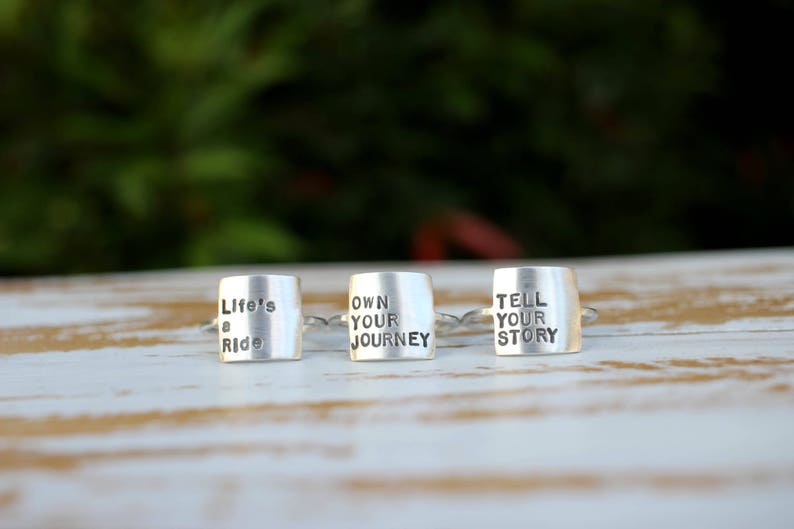 K&ouml;nnte beinhalten: Drei silberne Ringe mit gravierten Botschaften: "Life's a Ride", "Own Your Journey" und "Tell Your Story".