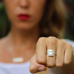 K&ouml;nnte beinhalten: Ein silberner Ring mit einem quadratischen Band, auf dem in einer einfachen Schrift "I CAN & I WILL" steht.