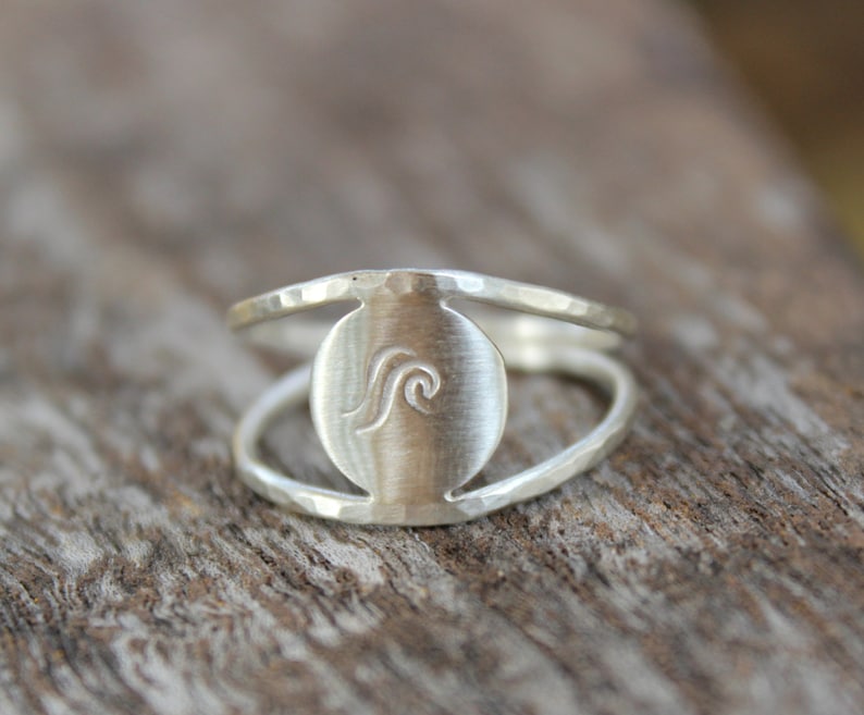 May include: A silver ring with a hammered finish and a circular cutout featuring a wave design.
