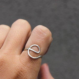 Op de afbeelding: Een zilveren ring met een gehamerde afwerking, in de vorm van de letter 'e'.