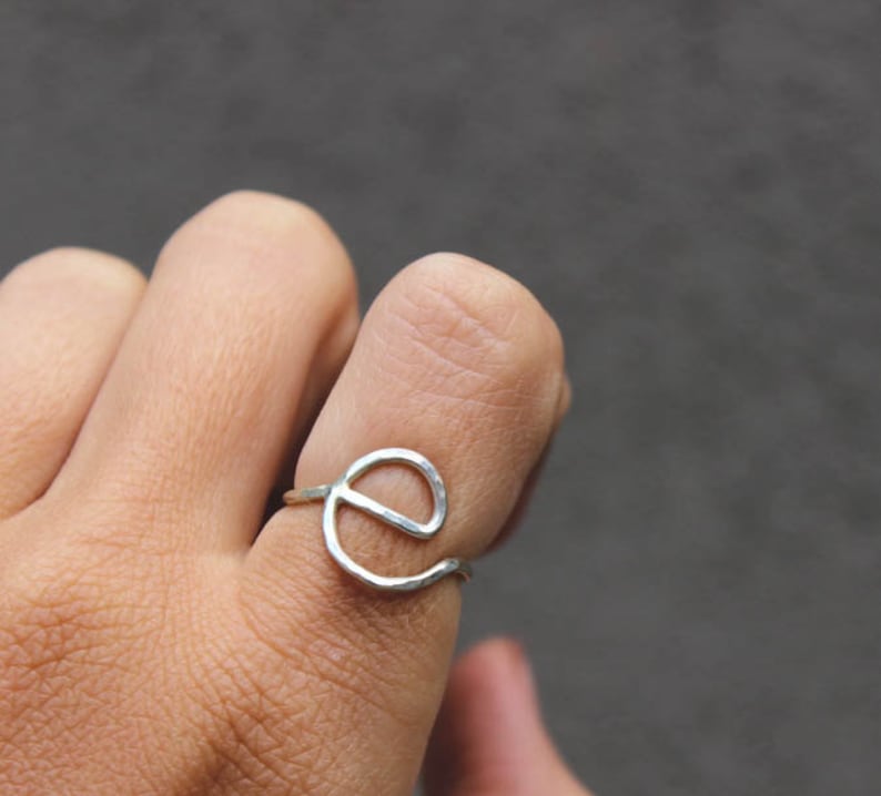 Op de afbeelding: Een zilveren ring met een gehamerde afwerking, in de vorm van de letter 'e'.