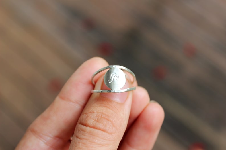 May include: A silver ring featuring a wave design on the front. The ring is open on the sides and has a hammered texture.