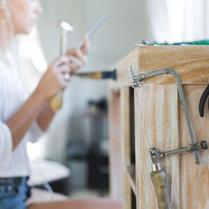 Op de afbeelding: Een close-up van een houten werkbank met een zilveren zaag, een tang en een pincet die aan de zijkant hangen.