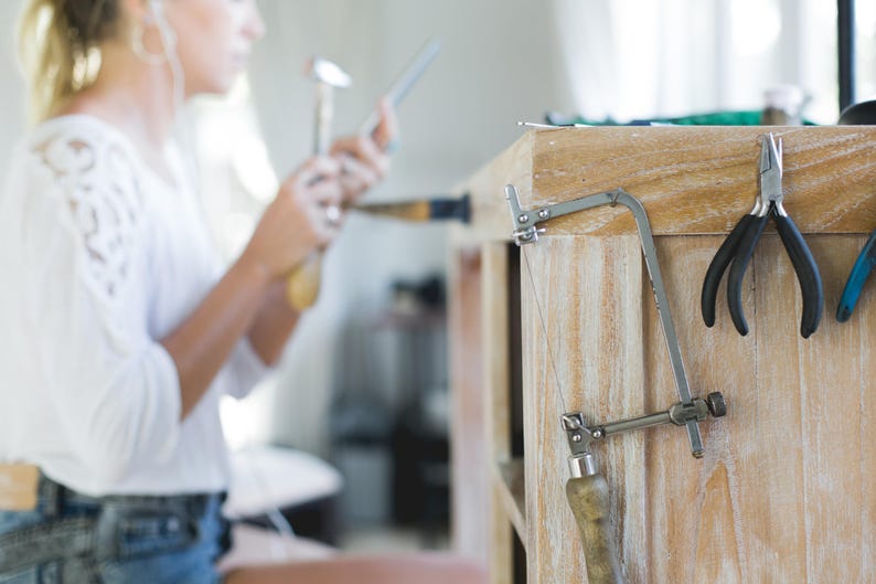 Op de afbeelding: Een close-up van een houten werkbank met een zilveren zaag, een tang en een pincet die aan de zijkant hangen.