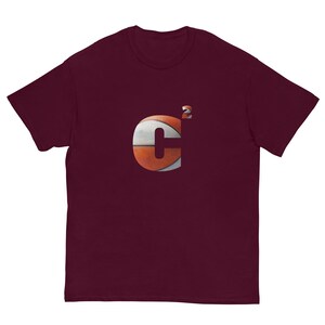 Puede incluir: Camiseta de manga corta color burdeos con un gráfico de baloncesto de la letra "C" con un superíndice "2".