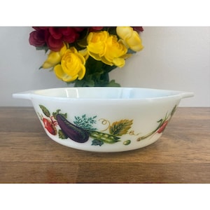 May include: White oval serving bowl with a colourful vegetable design. The bowl features illustrations of a red tomato, purple aubergine, green peas, and other vegetables. The bowl has two small handles.