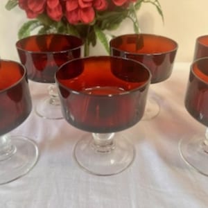 May include: Set of six red glass dessert dishes with clear glass stems. The dishes are round and have a slight lip. The stems are tall and slender.