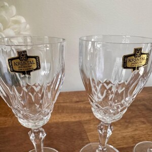 May include: Four clear glass wine glasses with a cut crystal design. Each glass has a gold label that reads "Kristal Zaječar 24% Lead"