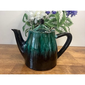 Puede incluir: Una taza de cerámica blanca con un asa negra y el texto "But First, Coffee" en negrita negra. La taza se encuentra sobre un fondo borroso, resaltando su diseño limpio.