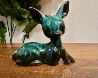May include: A green and brown glazed ceramic deer figurine. The deer is lying down with its head turned to the side. The glaze has a marbled effect.