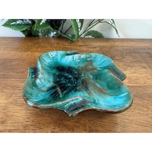 May include: A leaf-shaped ceramic dish with a glossy, teal and brown glaze. The dish has a unique, organic form with a dark center and a contrasting brown rim. This decorative piece is suitable for serving or display.