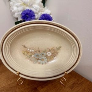 Puede incluir: Un juego de dos cuencos de cerámica ovalados con un diseño floral. Los cuencos son beige con un borde marrón y presentan un delicado patrón floral en tonos marrones, blancos y azules.