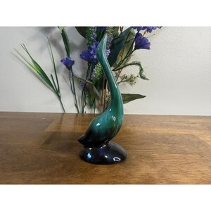 May include: A ceramic swan figurine featuring a glossy glaze that transitions from a deep, dark blue at the base to a vibrant emerald green along the elongated, curved neck and head, standing on a smooth, rounded pedestal base.