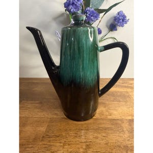 May include: A tall ceramic coffee pot featuring a glossy glaze that transitions from a deep dark brown at the base to a vibrant emerald green at the top. The vessel includes a long, slender spout, a curved handle, and a matching lid with a knob.